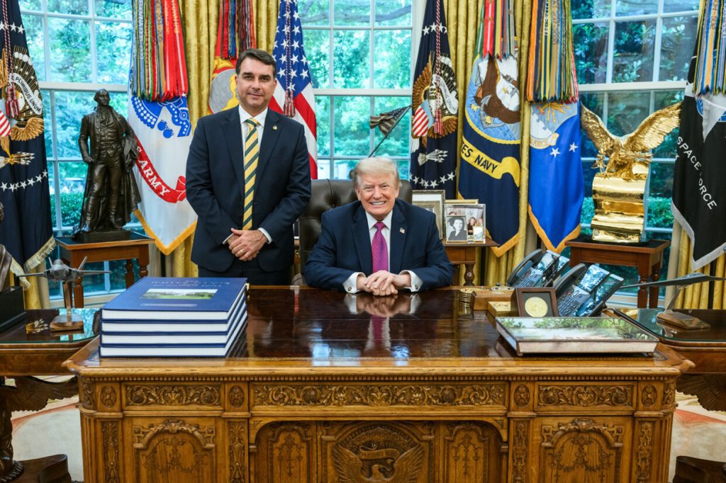 O senador brasileiro Flávio Bolsonaro em pé ao lado do ex-presidente norte-americano Donald Trump no Salão Oval da Casa Branca.