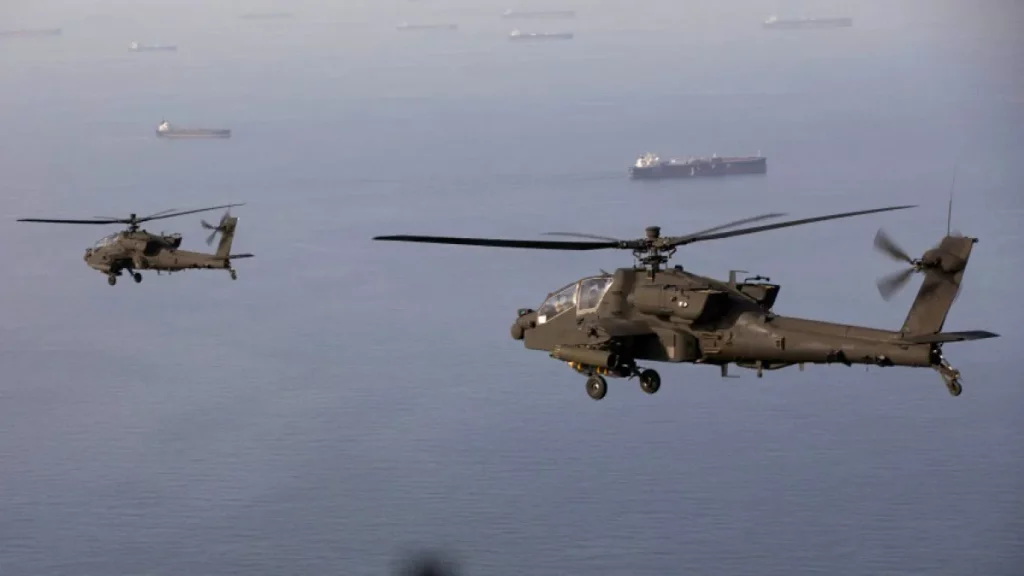 Helicópteros militares voam sobre o mar com navios ao fundo, próximo à região do Estreito de Hormuz. (Foto: aljazeera.com)