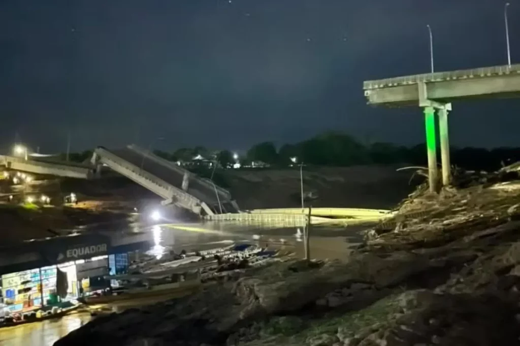 Ponte desabada no Acre é vista à noite, com estrutura parcialmente submersa e loja próxima iluminada. (Foto: metropoles.com)