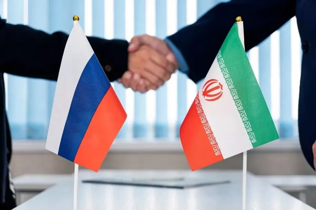 Dois homens apertam as mãos em frente às bandeiras da Rússia e do Irã. (Foto: en.mehrnews.com)