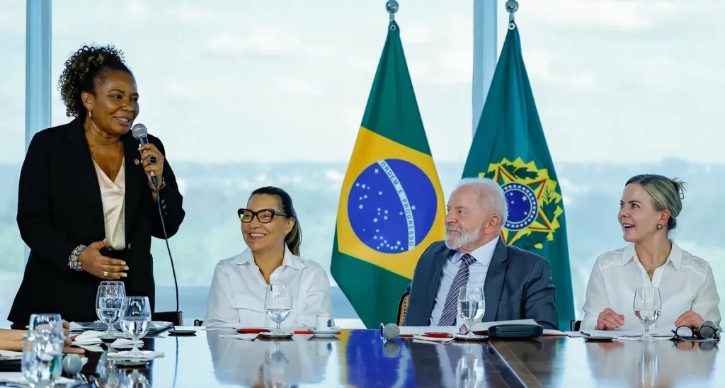 Mulher discursa em reunião com bandeiras do Brasil ao fundo. (Foto: Wikimedia Commons)
