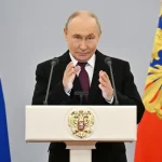 O presidente russo Vladimir Putin discursa em evento oficial com bandeiras nacionais ao fundo. (Foto: rt.com)