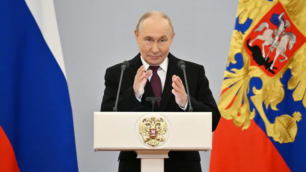 O presidente russo Vladimir Putin discursa em evento oficial com bandeiras nacionais ao fundo. (Foto: rt.com)