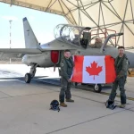 Pilotos da RCAF posam com a bandeira canadense ao lado de um avião na Base da Força Aérea Italiana Decimomannu. (Foto: defesa