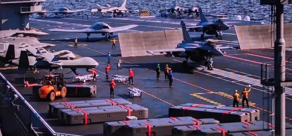 Tripulação trabalha na convés de um porta-aviões com aeronaves estacionadas. (Foto: navalnews.com)