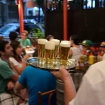 Garçom serve cervejas em um bar movimentado no Rio de Janeiro. (Foto: https://www.ocafezinho.com/2026/04/17/vida-noturna-no-b