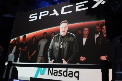 Elon Musk discursa em evento da SpaceX, com imagem de equipe ao fundo. (Foto: techcrunch.com)