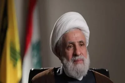 Sheikh Naim Qassem, líder do Hezbollah, em foto oficial com bandeiras do movimento ao fundo. (Foto: en.mehrnews.com)