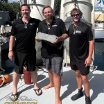 Três membros da equipe Mel Fisher's Shipwreck Expeditions exibem uma barra de prata recuperada do naufrágio do Atocha, em Key