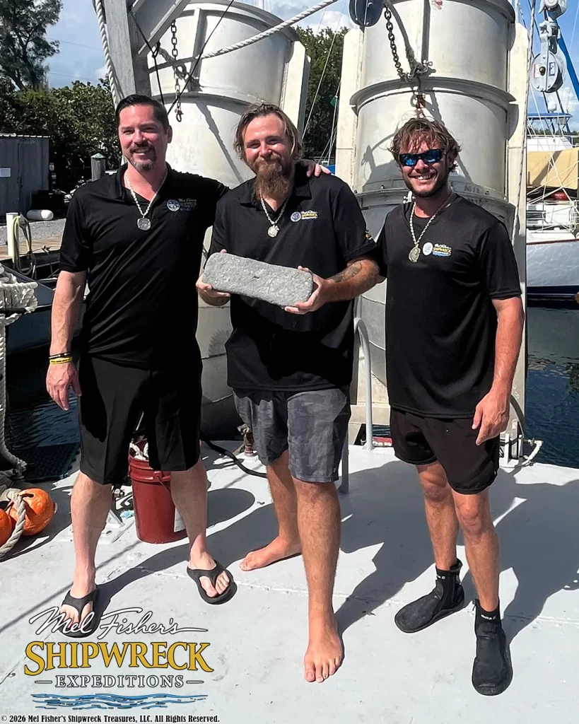 Três membros da equipe Mel Fisher's Shipwreck Expeditions exibem uma barra de prata recuperada do naufrágio do Atocha, em Key