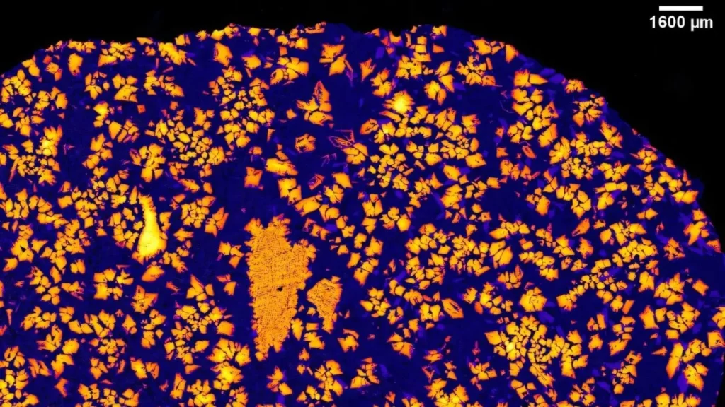 Detalhe microscópico de uma amostra de meteorito, mostrando estruturas cristalinas em tons de laranja e azul. (Foto: www.pops
