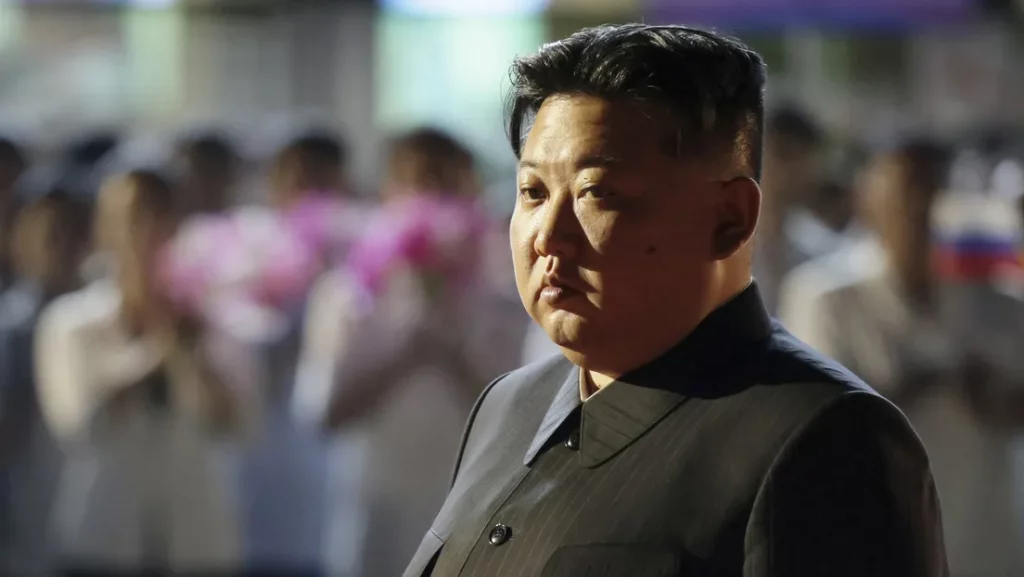 Kim Jong-un em evento público, com pessoas ao fundo segurando flores. (Foto: actualidad.rt.com)