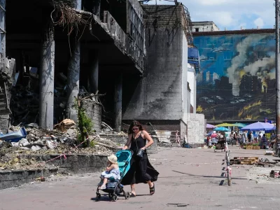 Mulher empurra carrinho com criança em rua destruída por bombardeios em cidade ucraniana. (Foto: aljazeera.com)