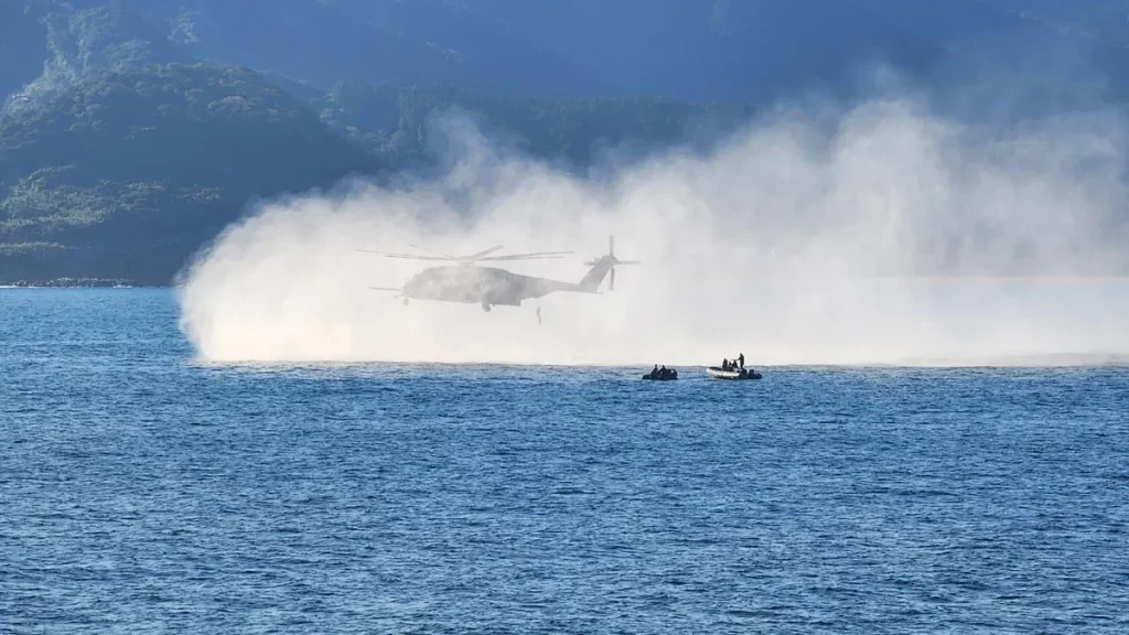 Um helicóptero da Marinha dos EUA realiza operação de mineração em águas costeiras, com embarcações ao lado. (Foto: navalnews