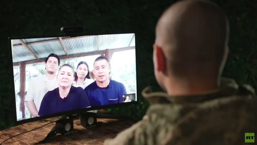 Um homem em uniforme assiste a uma videochamada com sua família, que aparece na tela. (Foto: rt.com)
