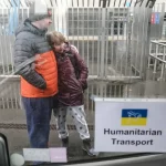 Um casal de refugiados ucranianos aguarda transporte humanitário em local externo. (Foto: rt.com)