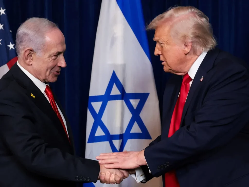 Trump e Netanyahu se cumprimentam com aperto de mão em frente às bandeiras dos EUA e Israel. (Foto: aljazeera.com)
